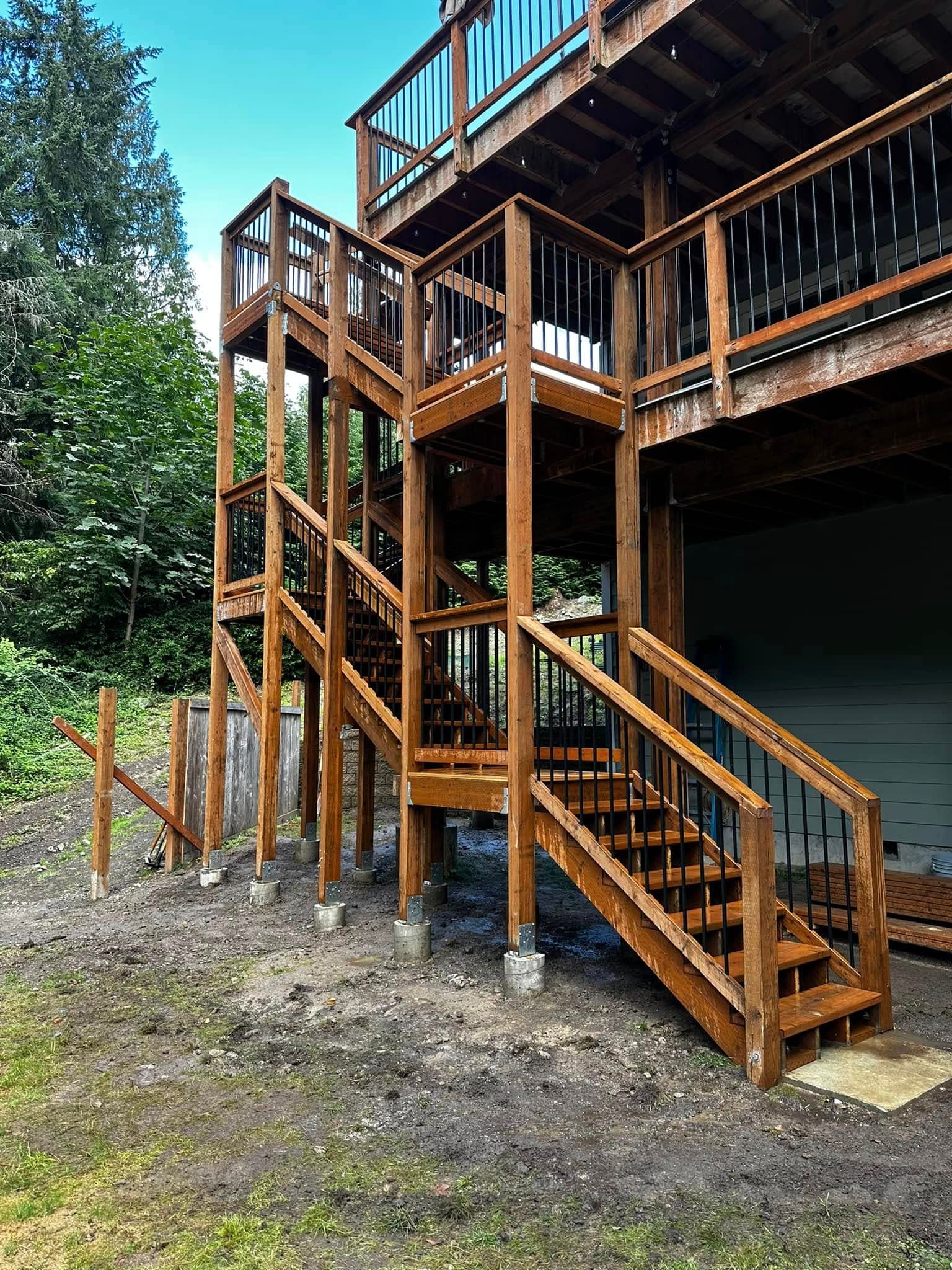 Multi-story stained wood deck with custom staircase set against Pacific Northwest forest